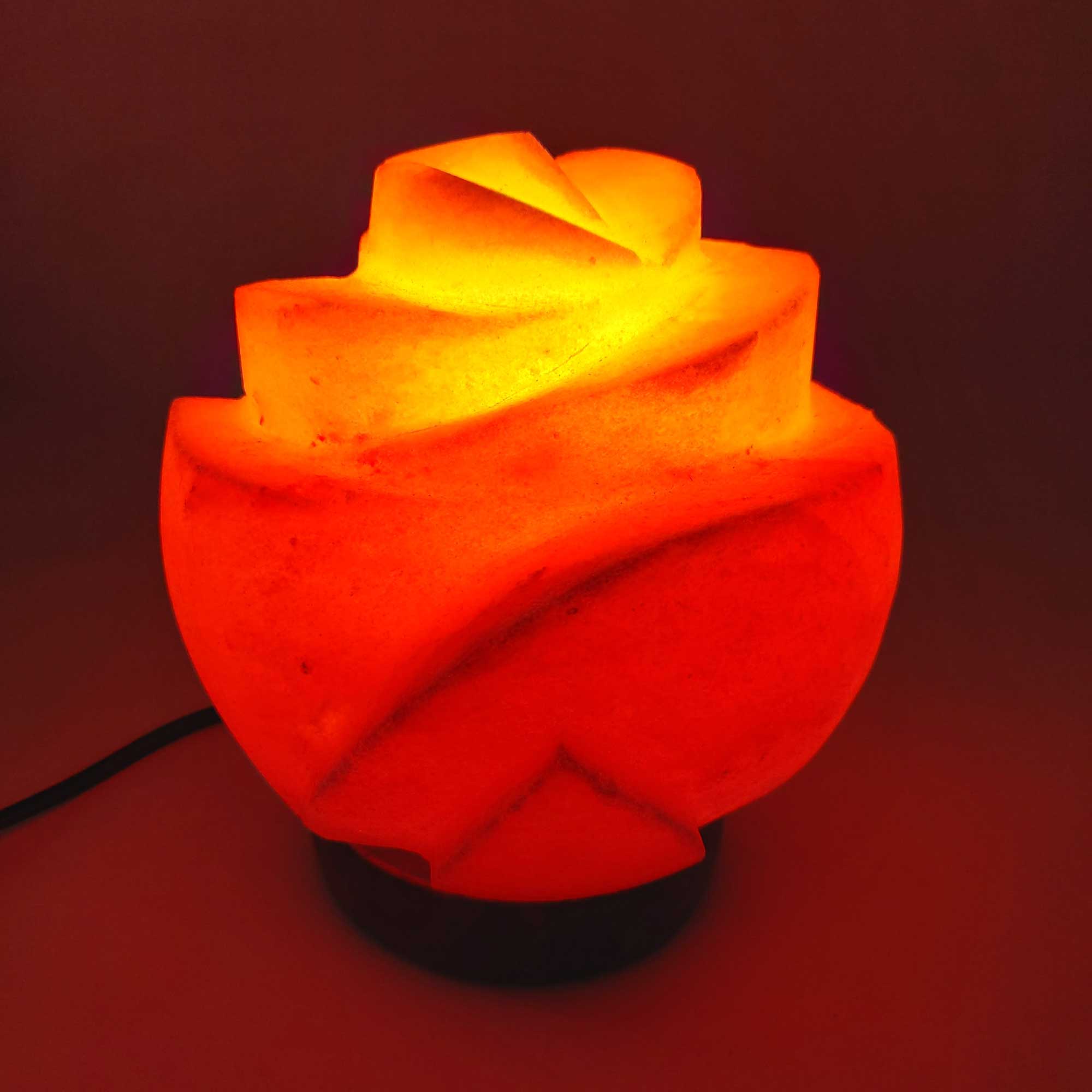 Flower-shaped carved salt lamp on wooden base, glowing warm pink