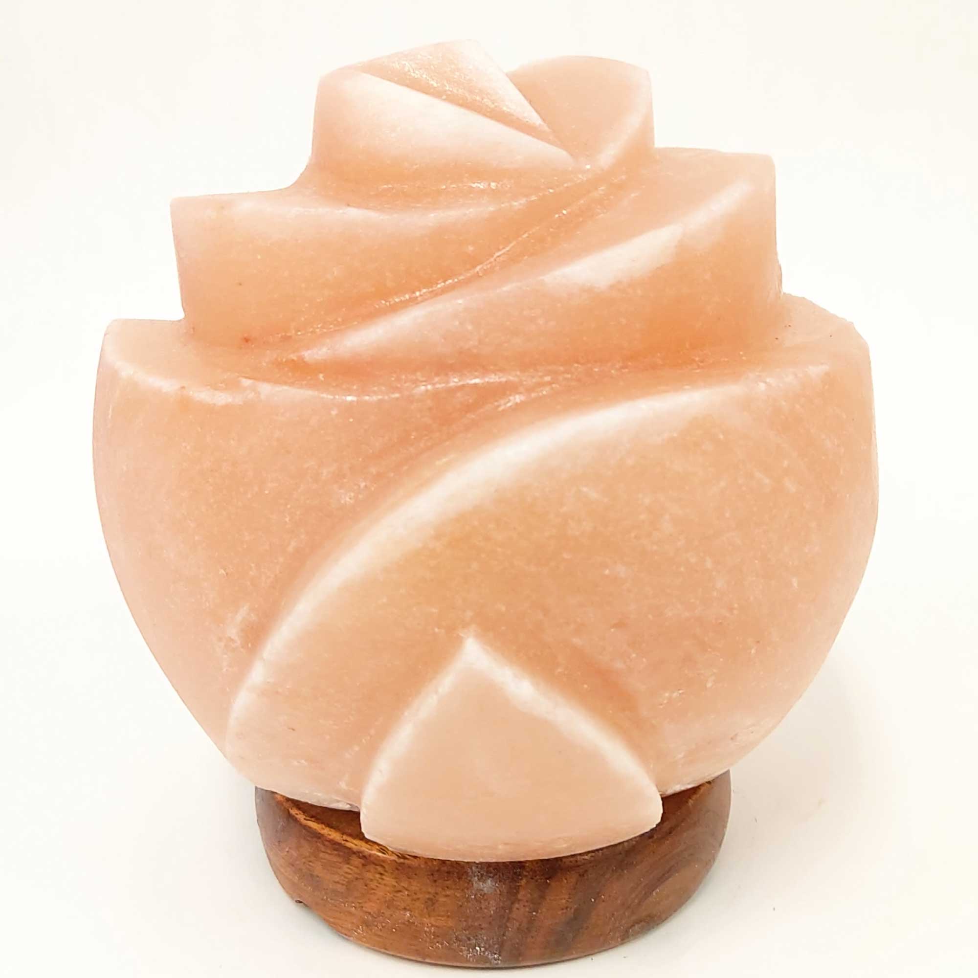 Side view of carved pink salt lamp in flower design on dark wooden base, unlit