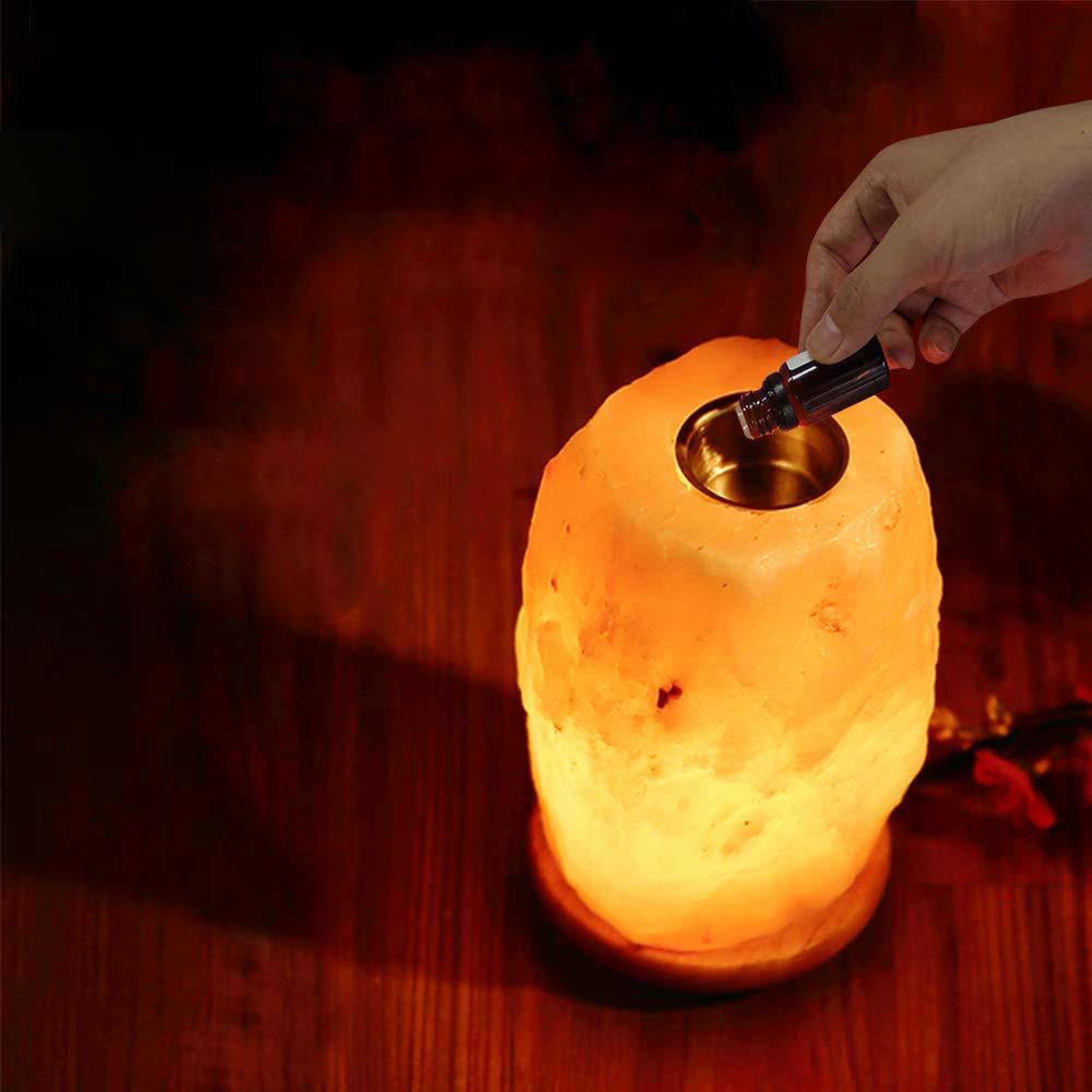 Himalayan salt diffuser lamp lit orange on tabletop as dropper is inserted