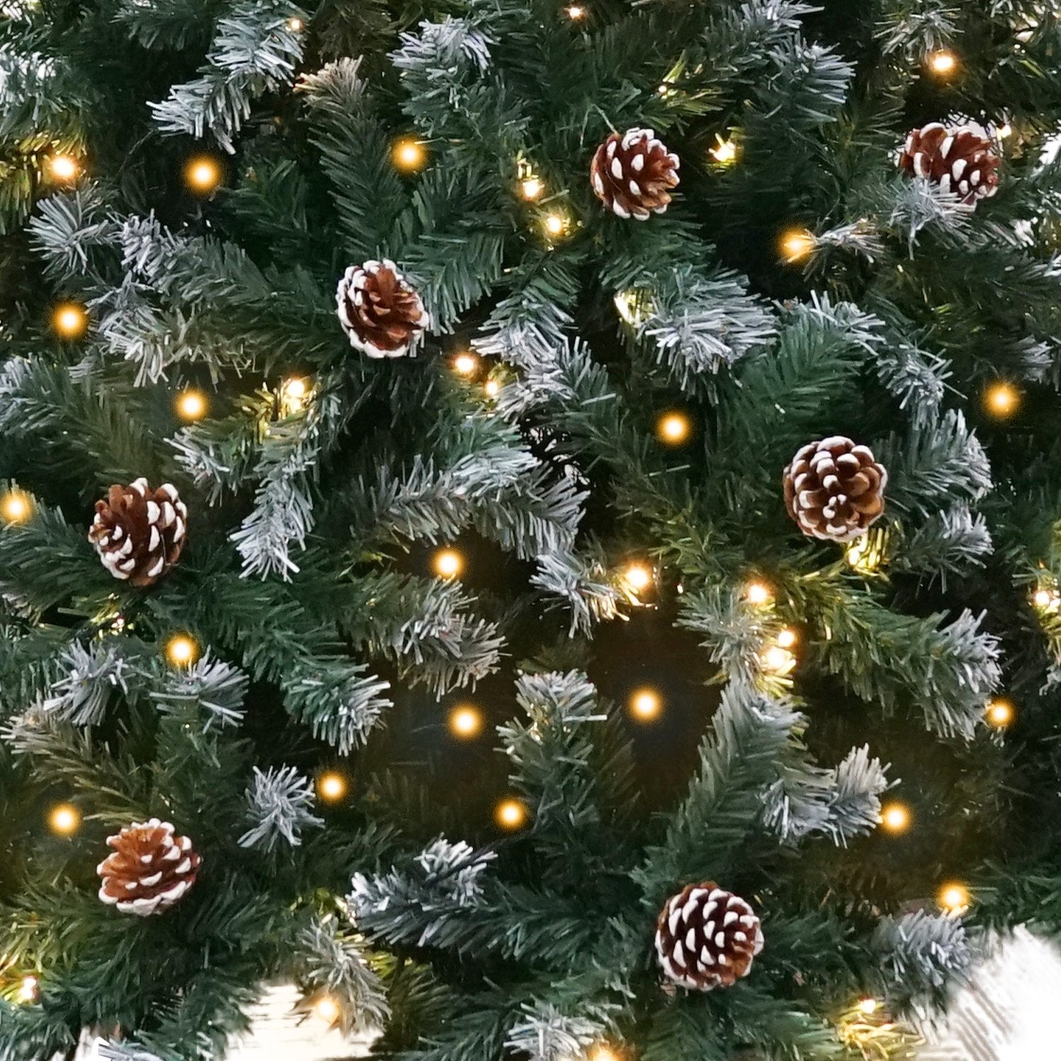 Pre-lit Christmas tree close-up with pine cones and glowing yellow LED lights