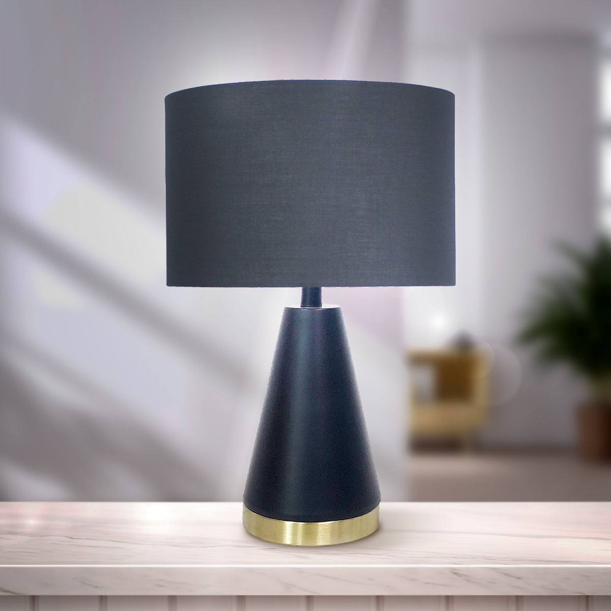 Black fabric drum table lamp with tapered metal base and gold bottom ring.