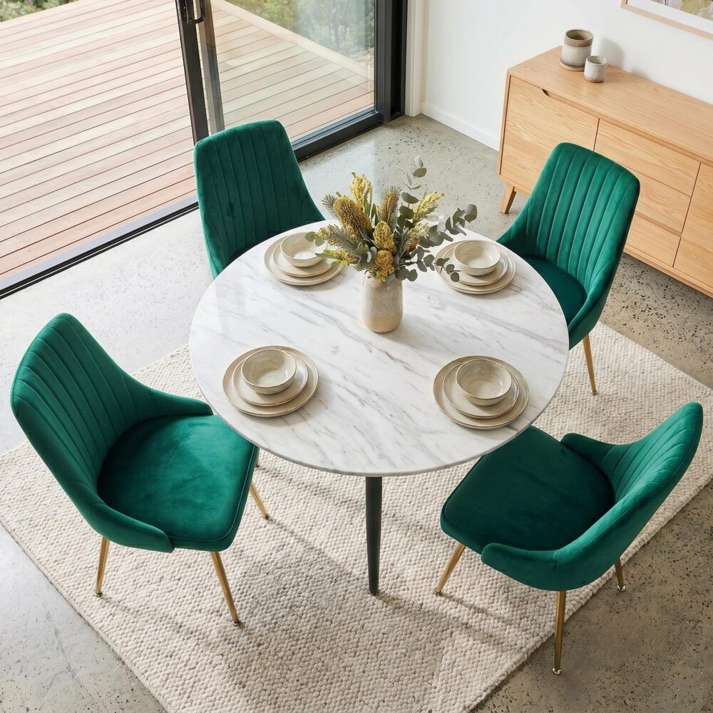 Round dining table with white top and black legs, surrounded by 4 green velvet chairs