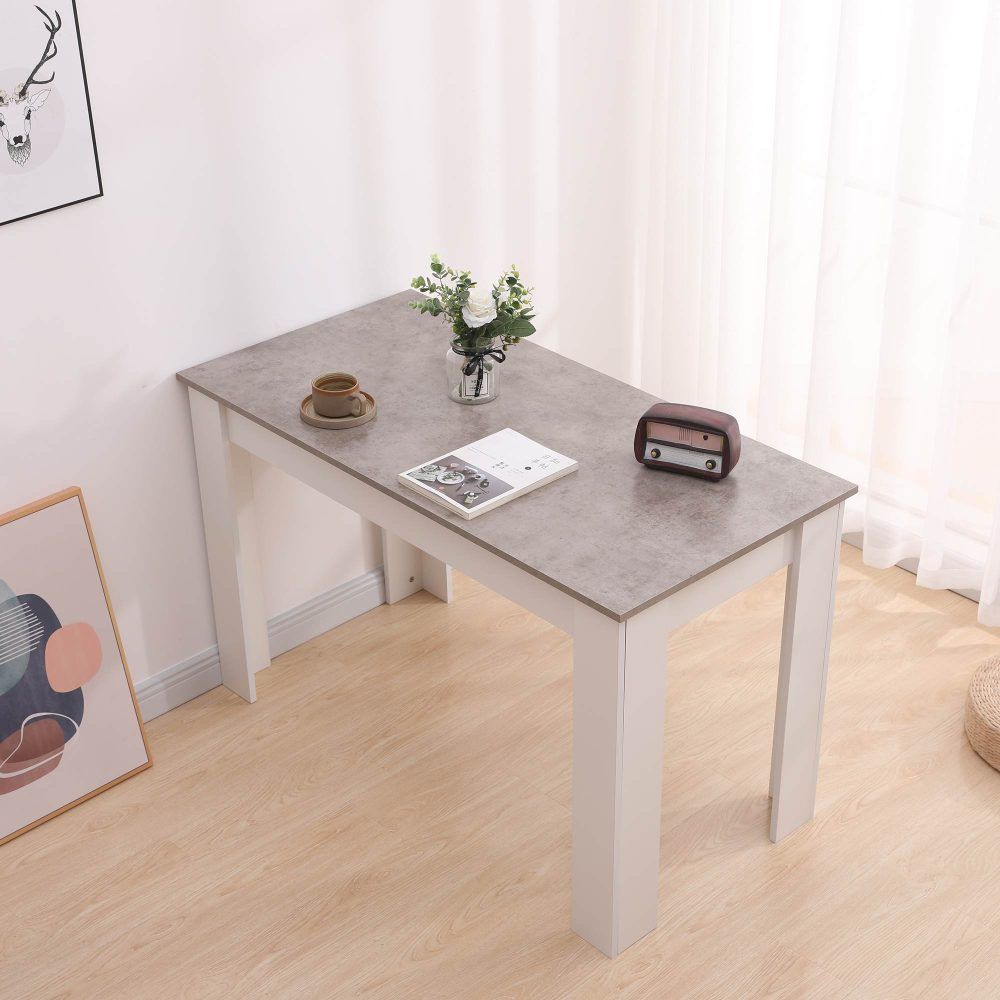 Rectangular dining table with grey tabletop and white legs, centerpiece and magazine on top