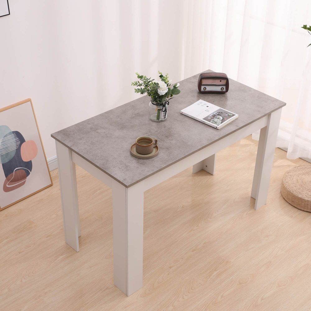 Rectangular dining table with grey surface and white legs, flowers and cup on tabletop