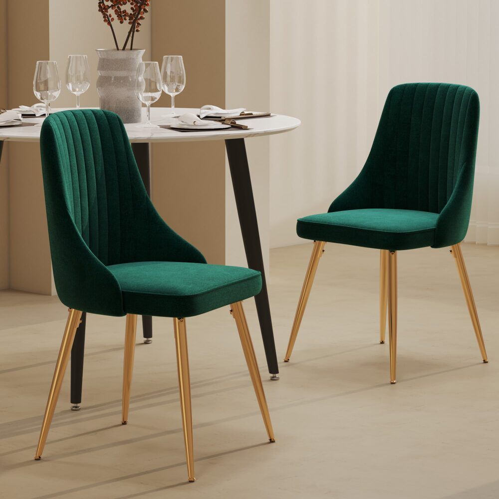 Two teal velvet dining chairs with gold legs and a dark round dining table