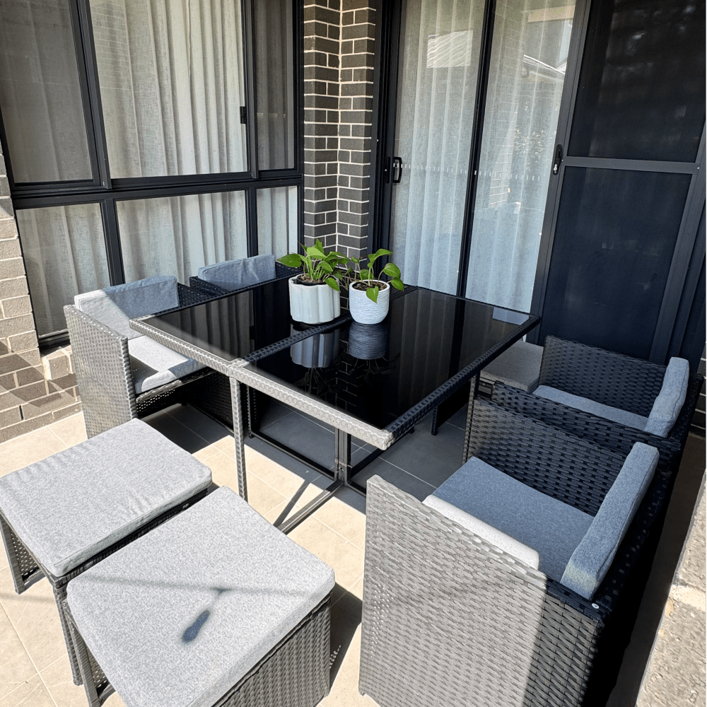 Outdoor dining set with black glass-top table, woven side chairs, and gray seat cushions