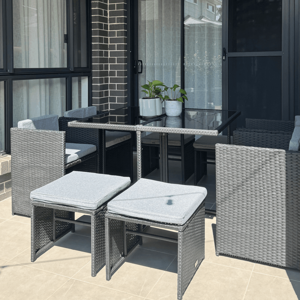 Outdoor dining set with black glass-top table and four woven chairs with gray cushions