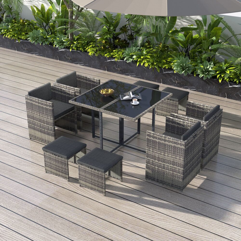 Outdoor dining set with grey woven rattan chairs, ottomans, and dark grey glass table