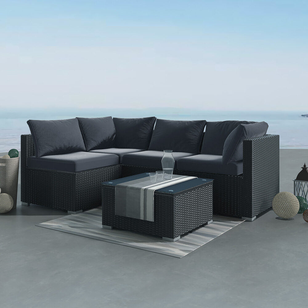 Outdoor modular lounge sofa set with black woven frame, dark gray cushions, and glass coffee table