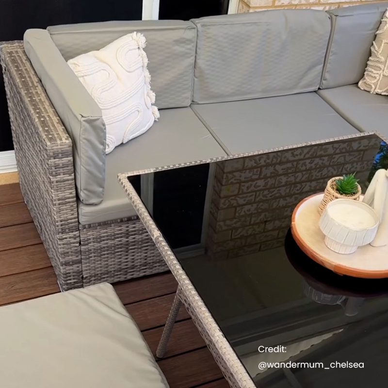 Grey wicker outdoor dining table with clear glass, beige cushions, and corner seating