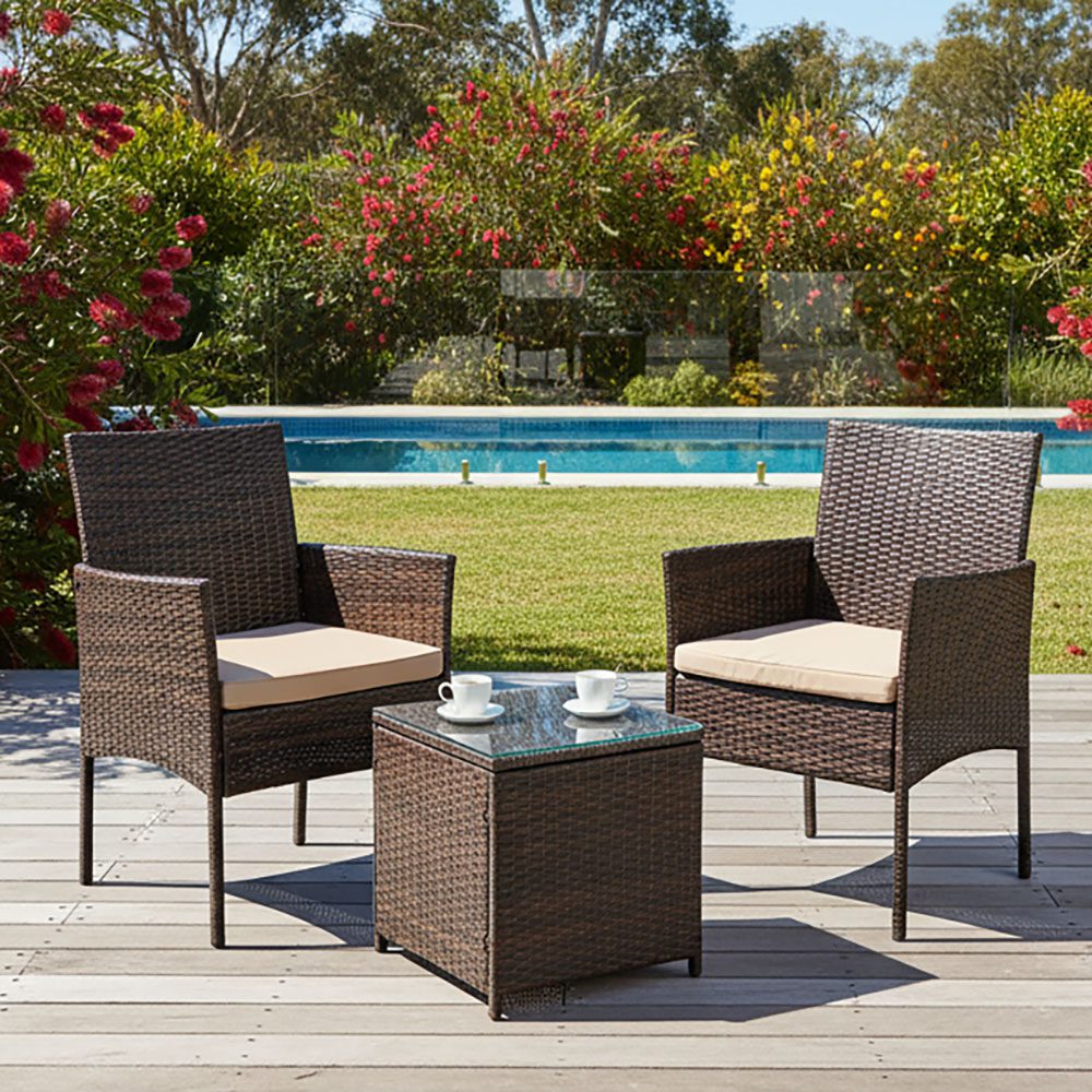 Outdoor bistro set with two dark wicker chairs, beige cushions, and square glass-top table