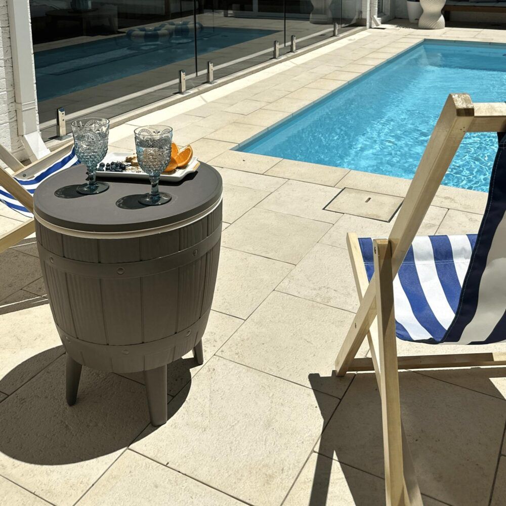Taupe round cooler table with built-in ice bucket and side table top on four legs.