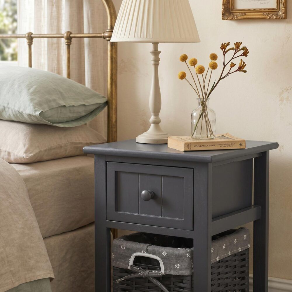 Grey bedside table with open wicker basket and drawer, styled with lamp and vase.