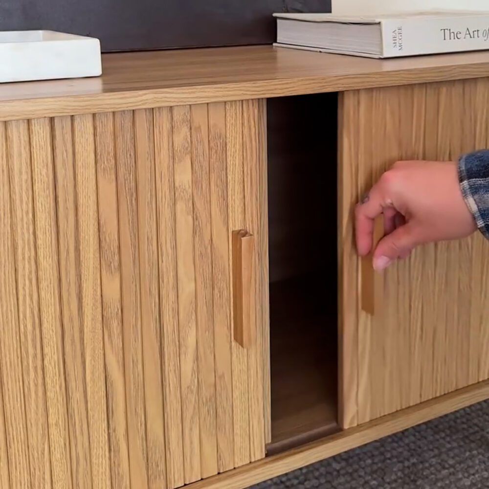 Wooden sideboard with ripple-grain panels and sliding door, open showing dark interior