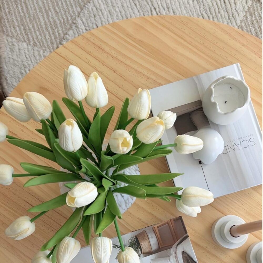 Natural wood coffee table with round top and slatted pedestal base, flowers on top