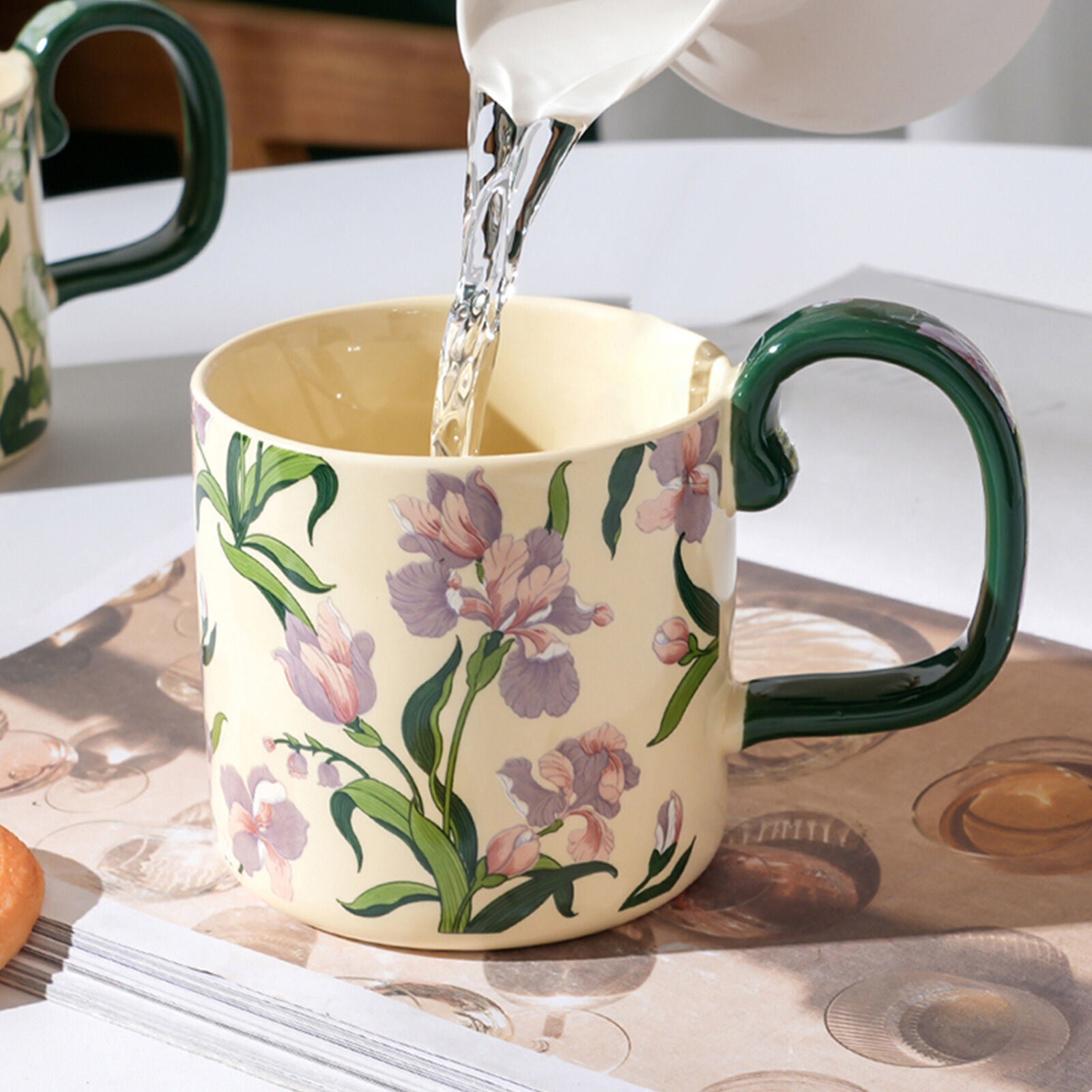 Ceramic porcelain mug with green handle as tea pours into the cup