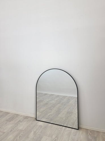 Arched wall mirror with black frame against light wall, full height view