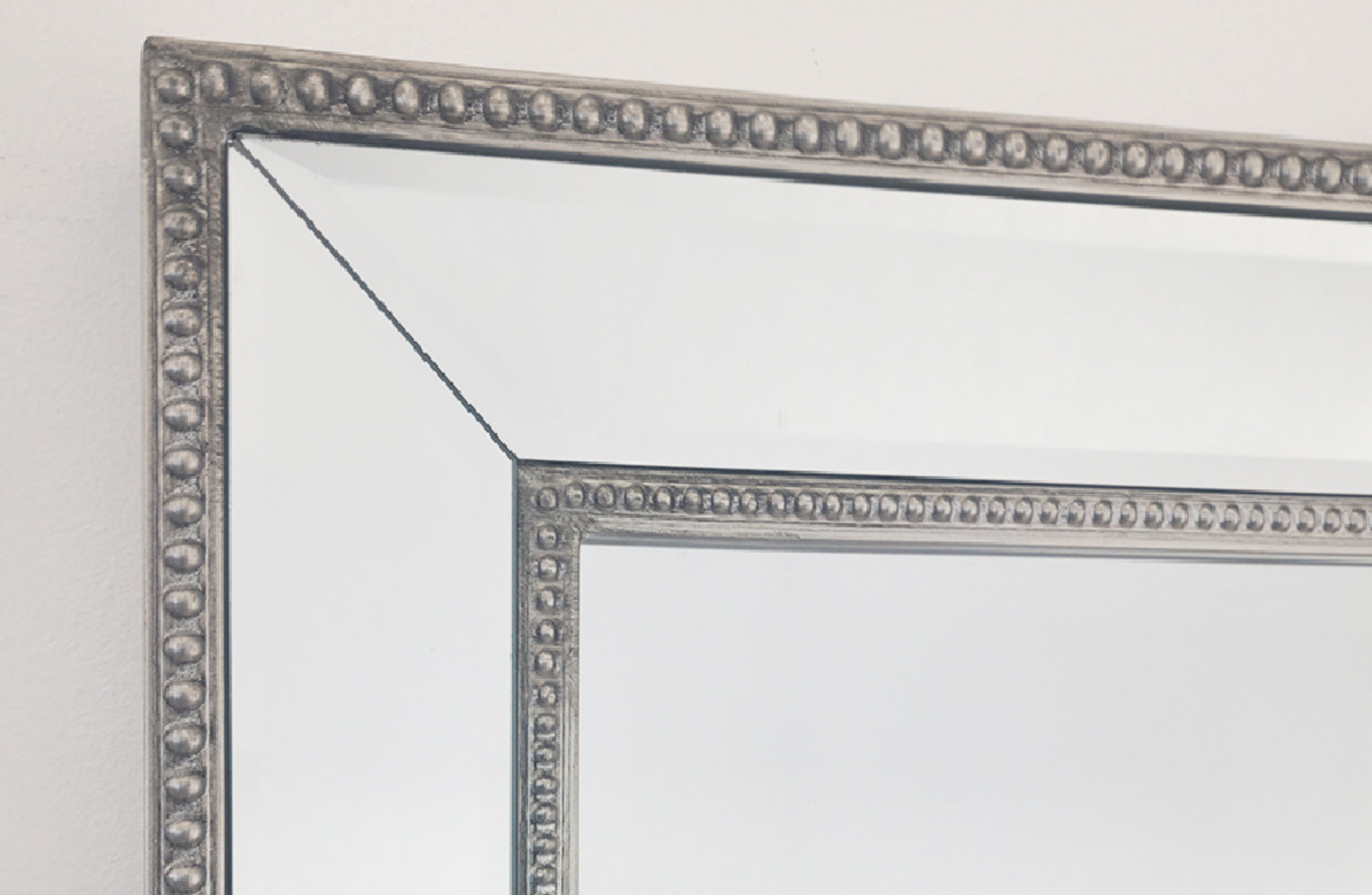 Corner view of silver beaded mirror frame with beveled edge and inner border