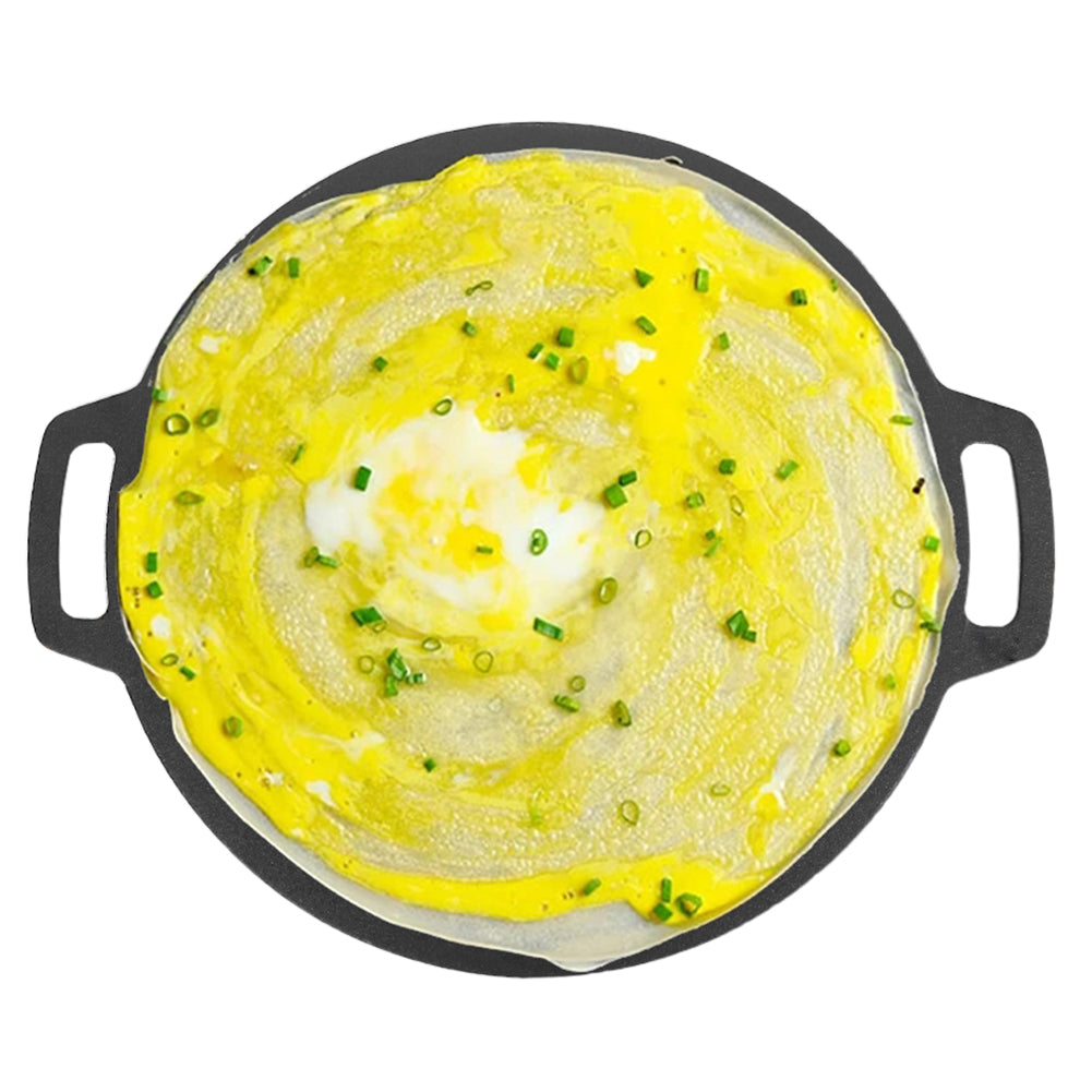 Round seasoned cast iron crepes pan with yellow crepe, herbs, and egg filling