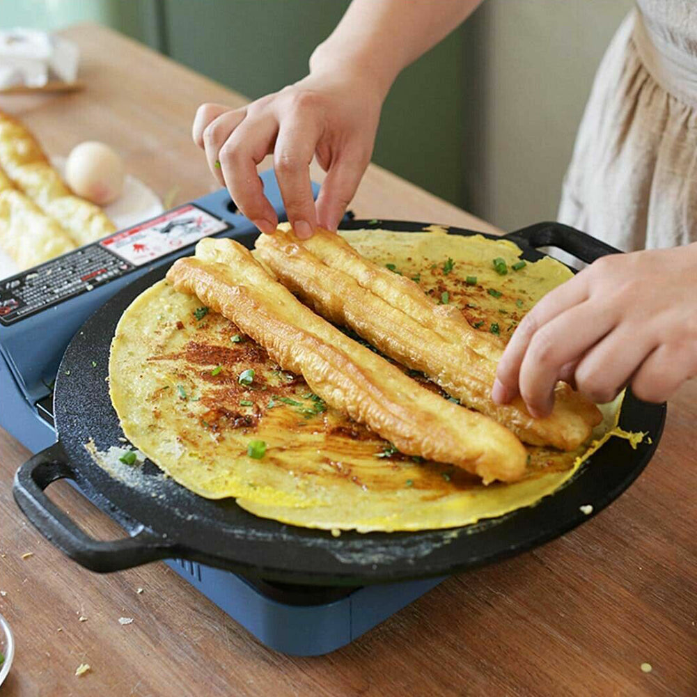 Seasoned cast iron crepes pan holding rolled yellow crepes, hands lifting one roll