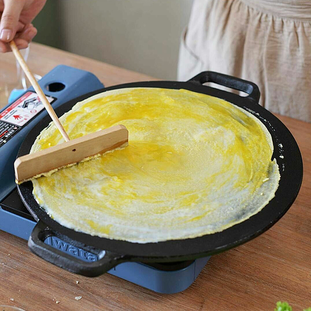 Seasoned cast iron crepes pan cooking a thin yellow crepe on a wooden table