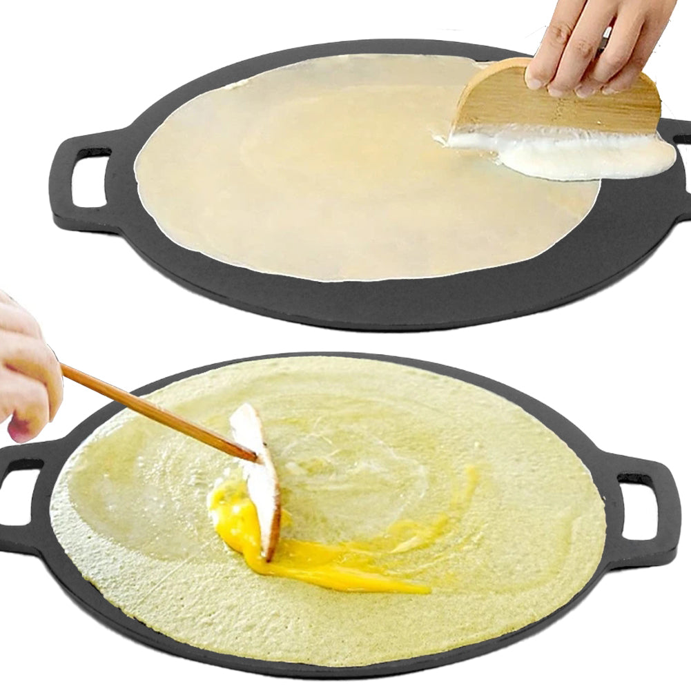Seasoned cast iron crepes pan with two crepes in progress, one being spread with a wooden tool