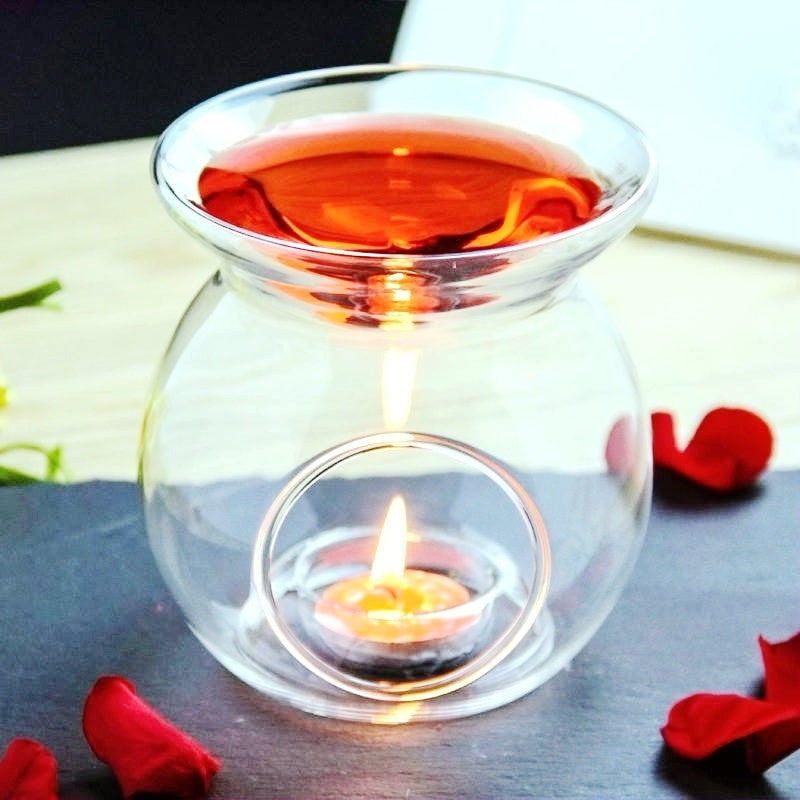 Glass tealight candle warmer with orange liquid top and lit tealight in round window