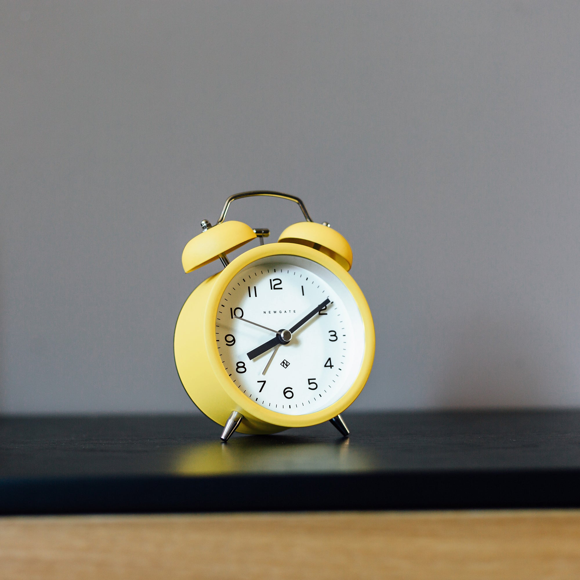 Yellow twin bell alarm clock standing on a tabletop with white face.