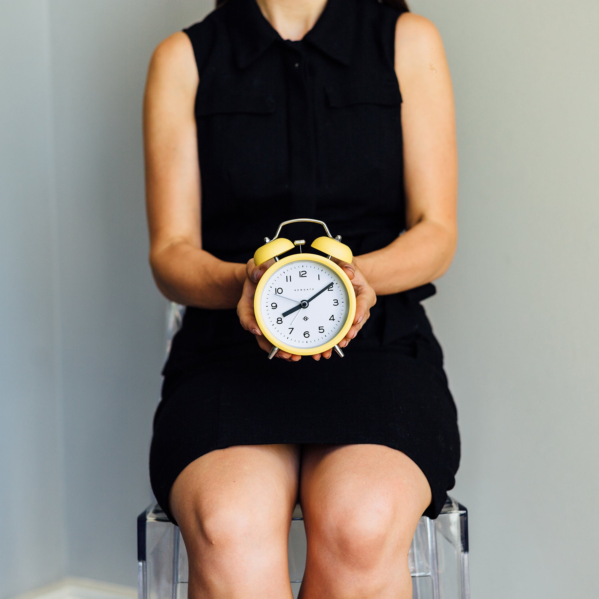 Yellow twin bell alarm clock held in hands; white dial with black numbers and hands.