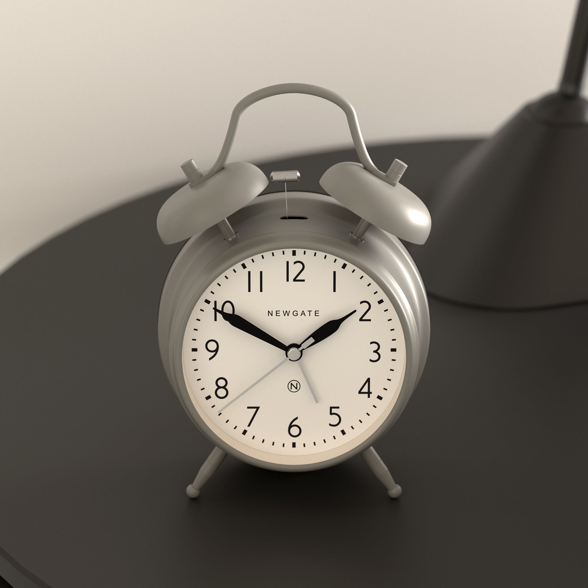 Silver-grey twin-bell alarm clock on two legs, close-up dial with black hands