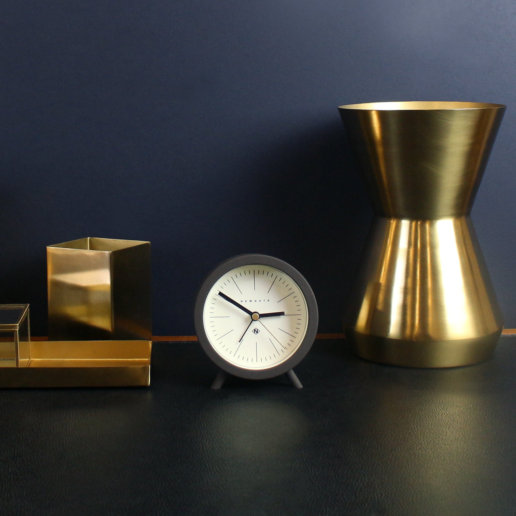 Mini alarm clock on surface with cream dial, black hands, and chocolate black case
