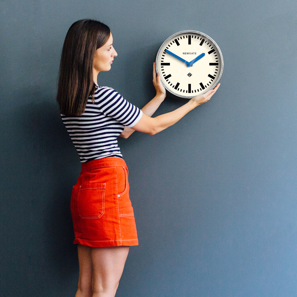 Wall clock on wall with cream face, black markers, and blue minute and hour hands