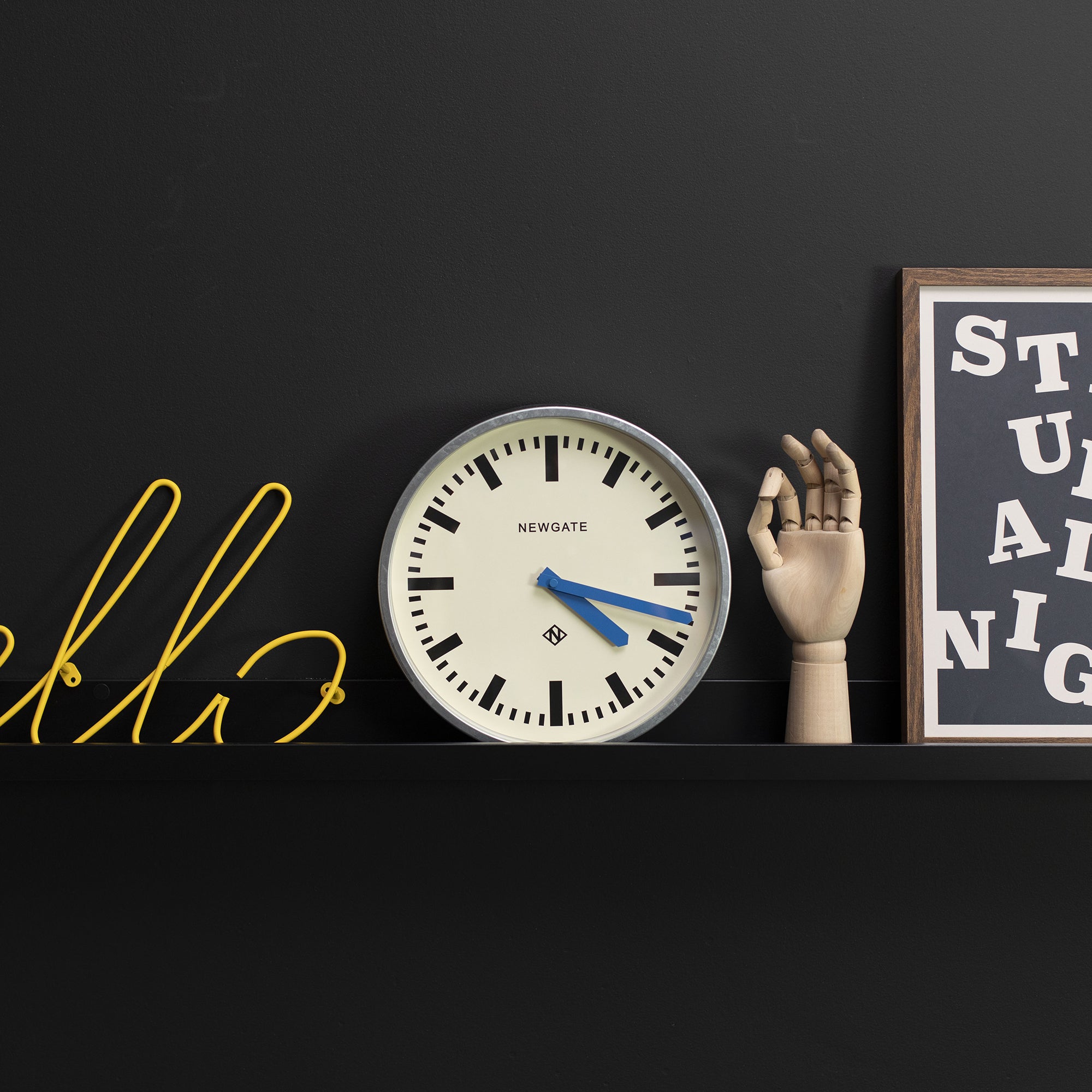 Wall clock on shelf with cream dial, black markers, and blue hands