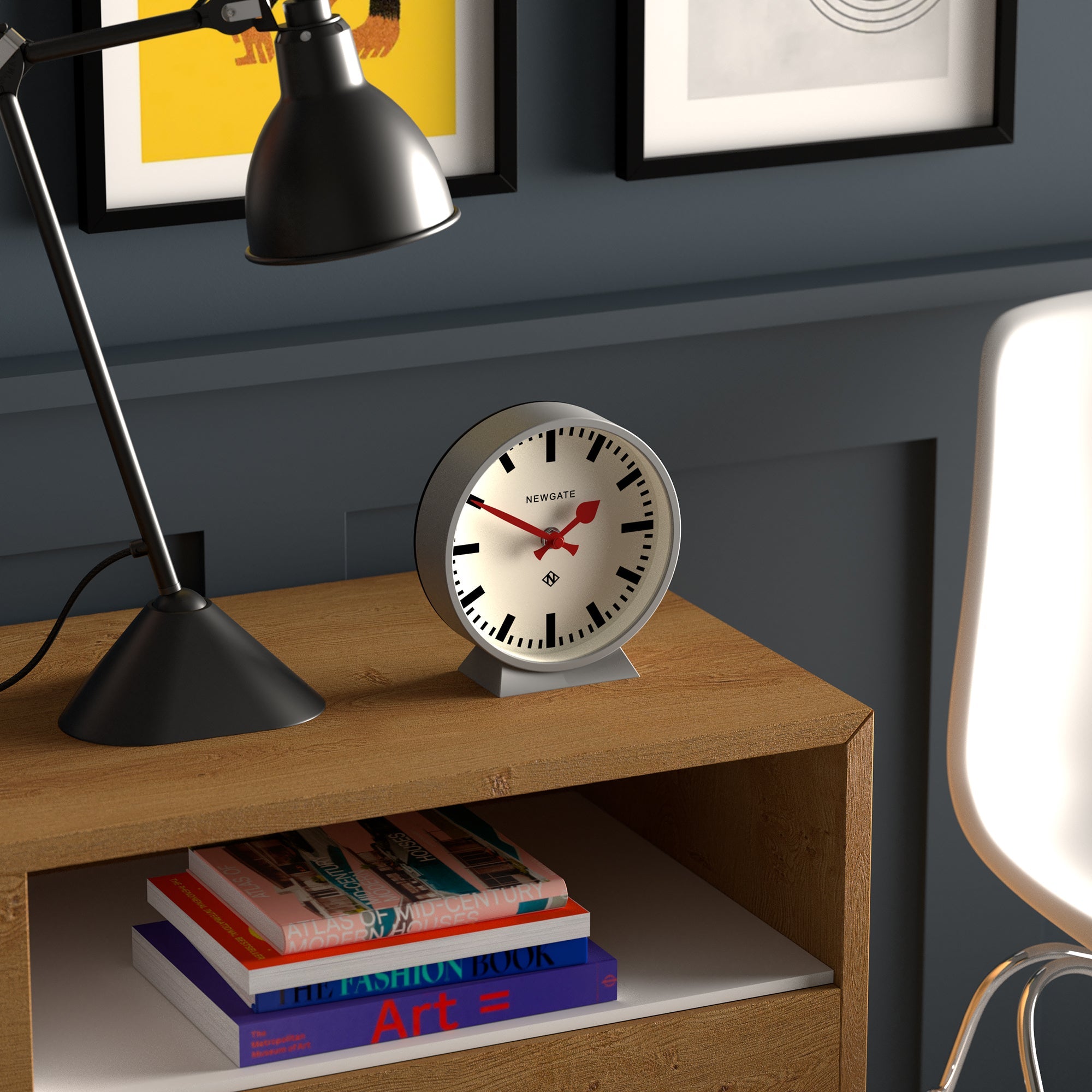 Small mantel clock with white face, red hands, black numerals, on grey base.