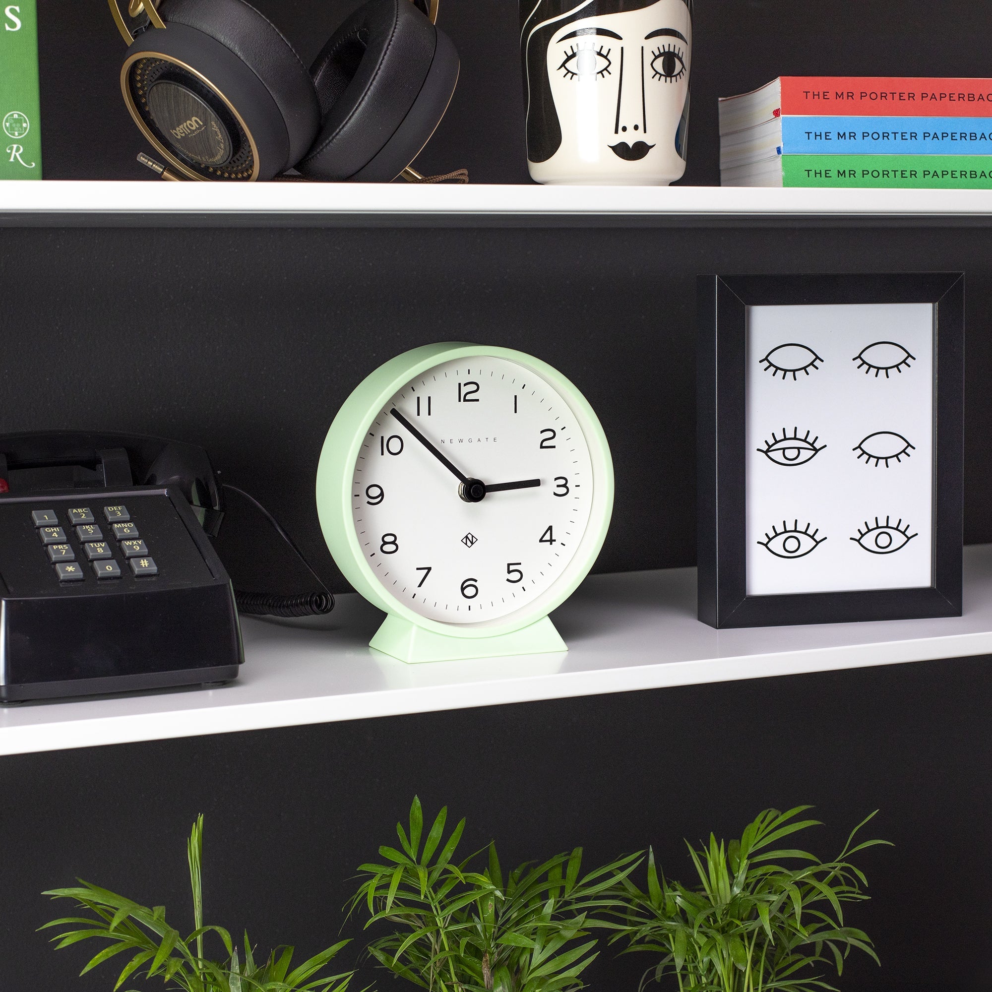 Mint round mantel clock on white shelf with black hands and arched stand