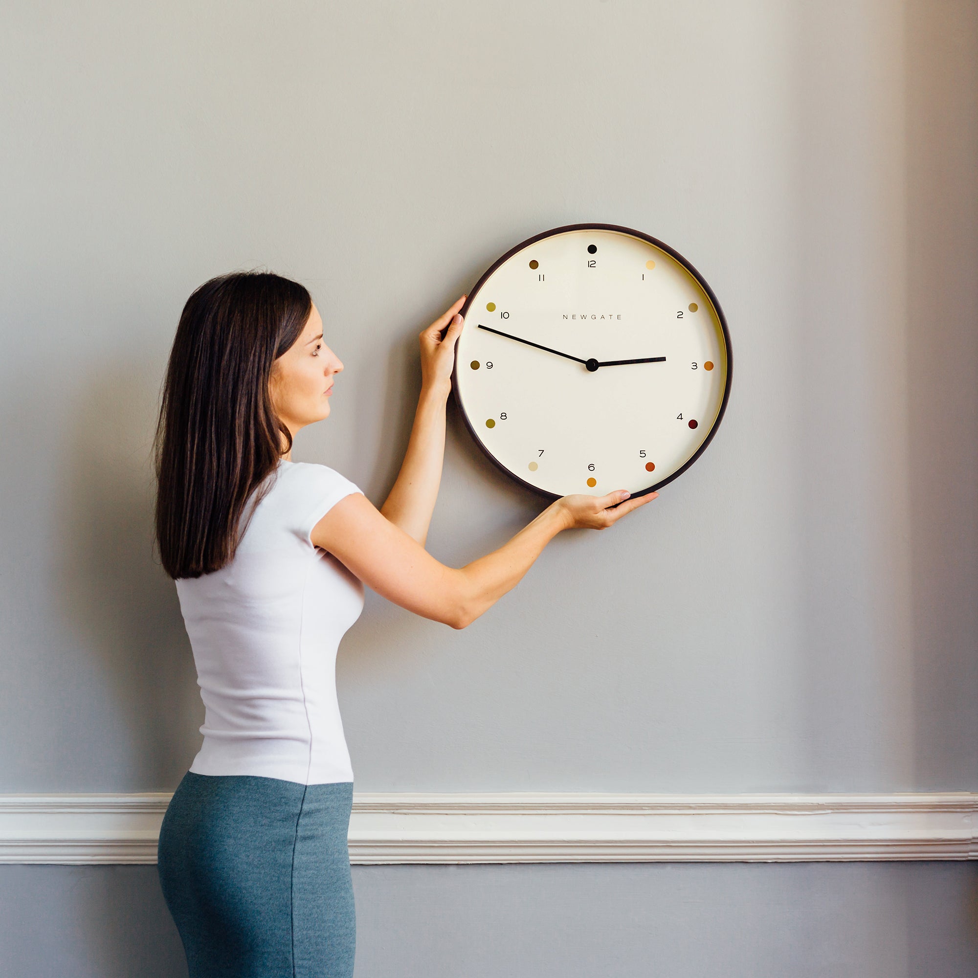 Wall-mounted round clock with cream dial, colored dot markers, and black hands
