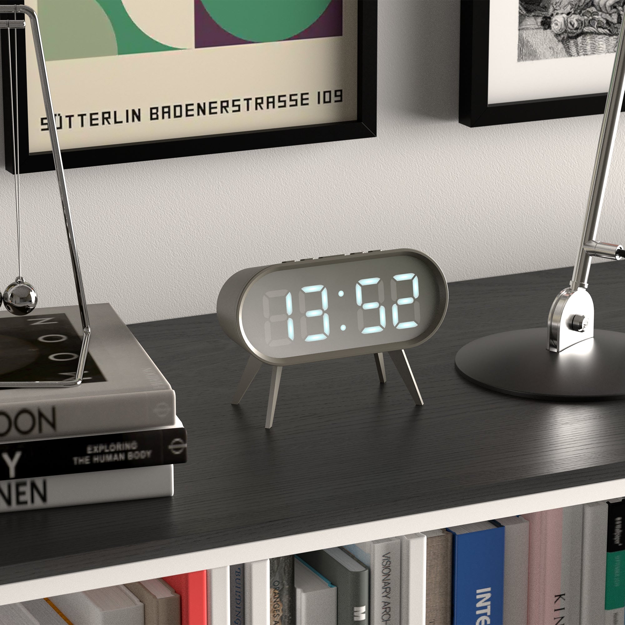 Grey LED alarm clock with digital time display 13:52, oval housing and tripod legs