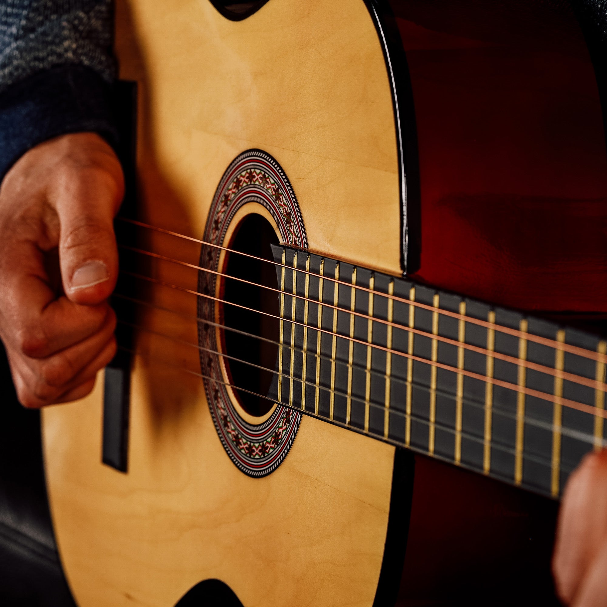 Natural classical guitar with decorative rosette, strings, and hand near sound hole
