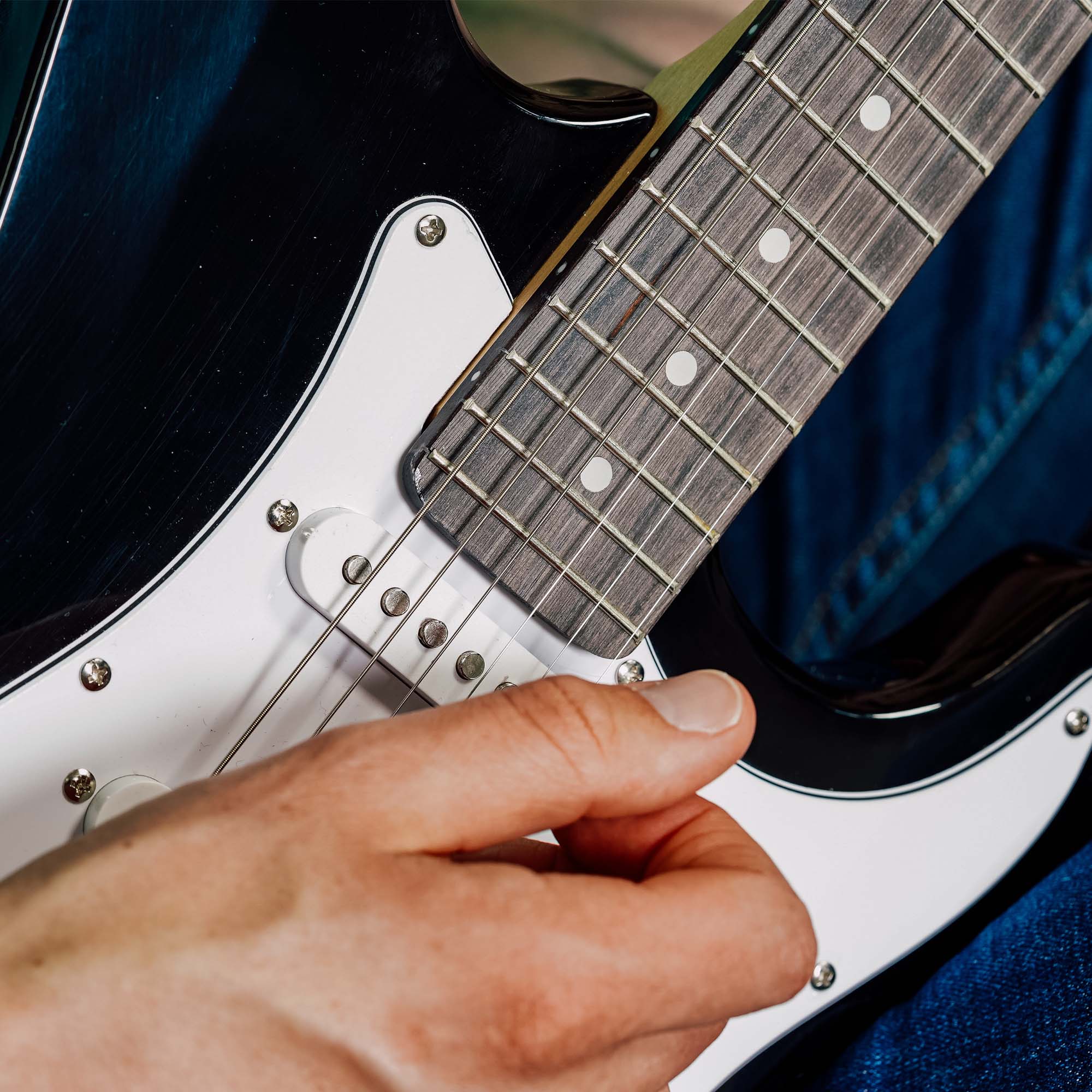 White electric guitar body and fretboard close-up with hand on strings