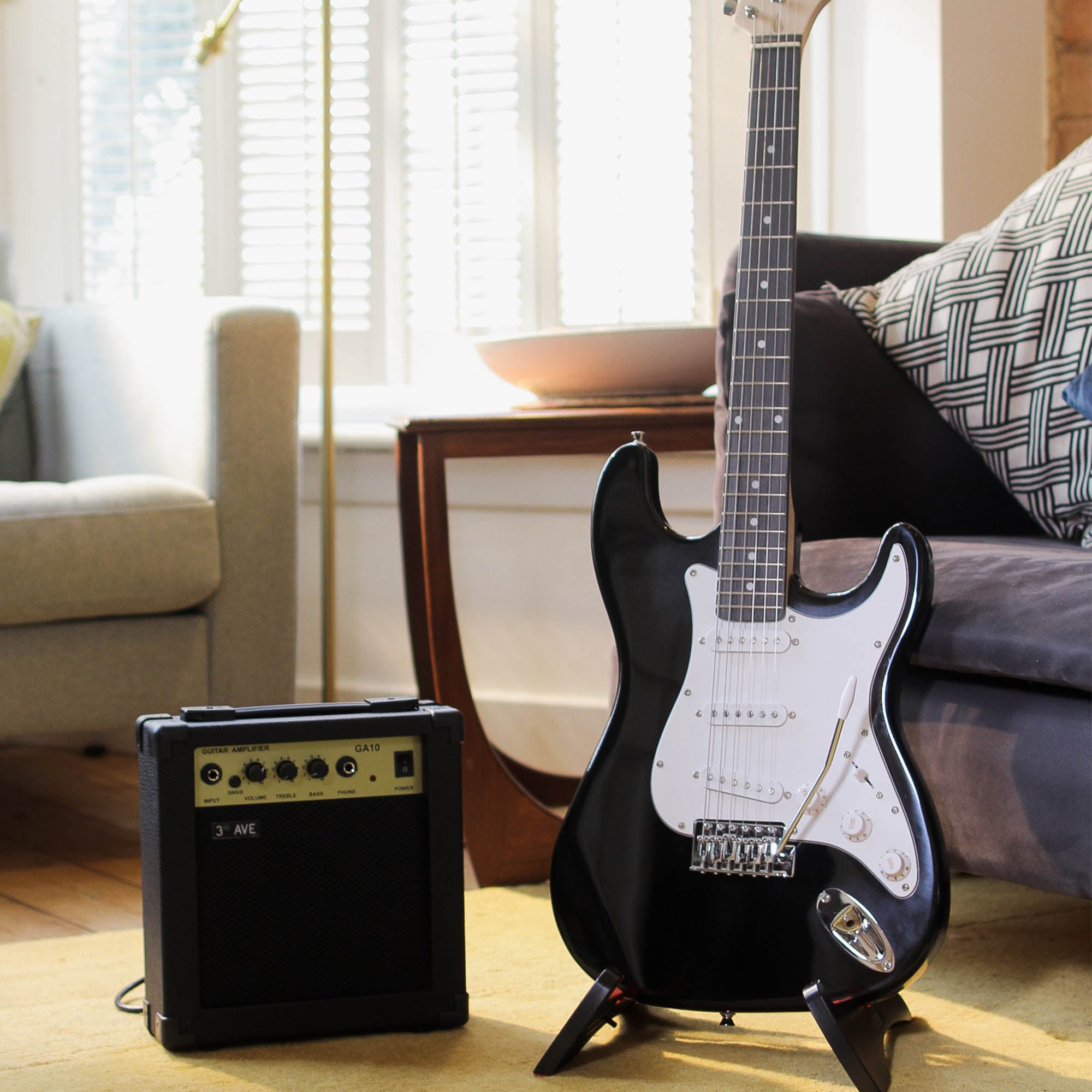 Black electric guitar on a stand with a small amp beside it