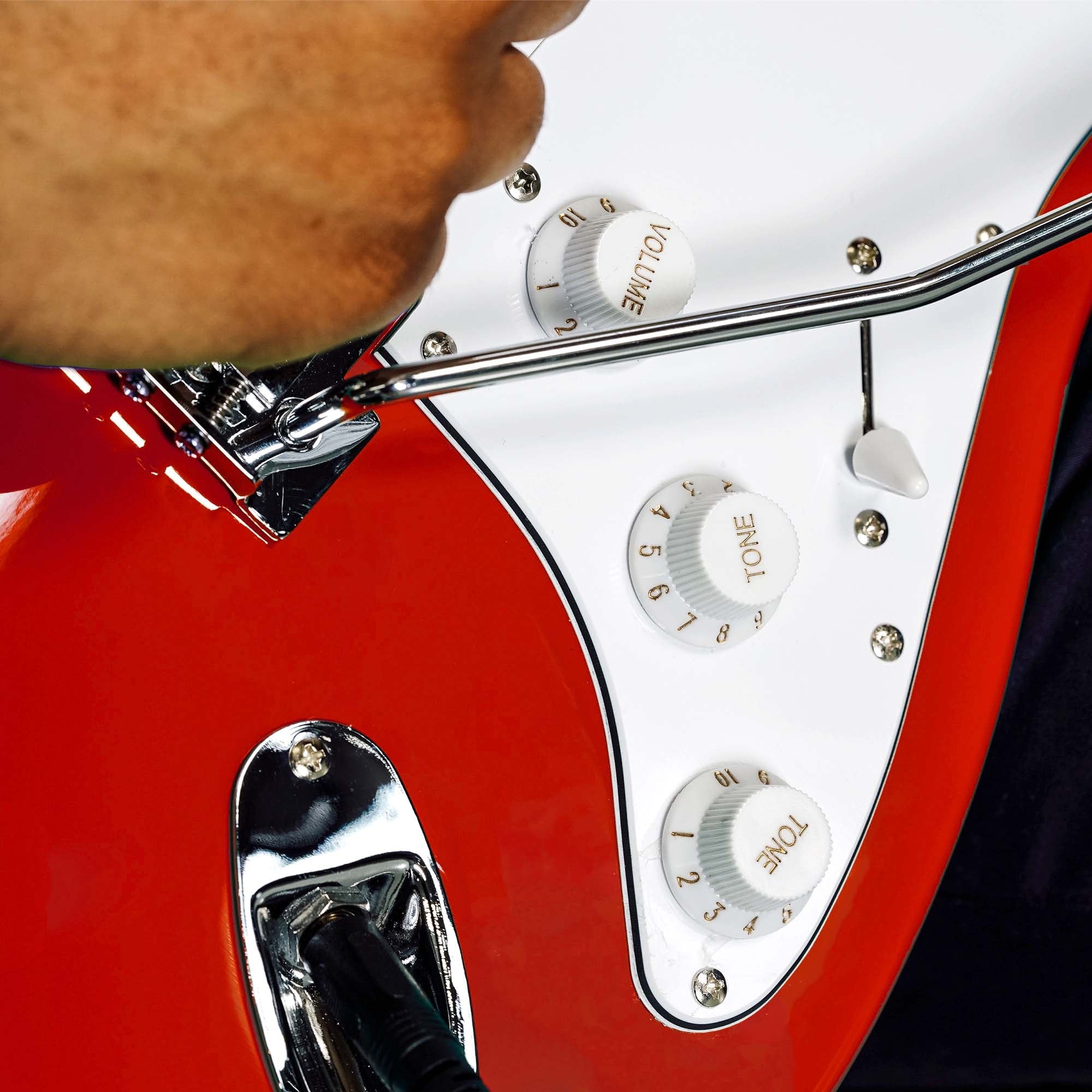 Close-up of red electric guitar control knobs and chrome pickup housing