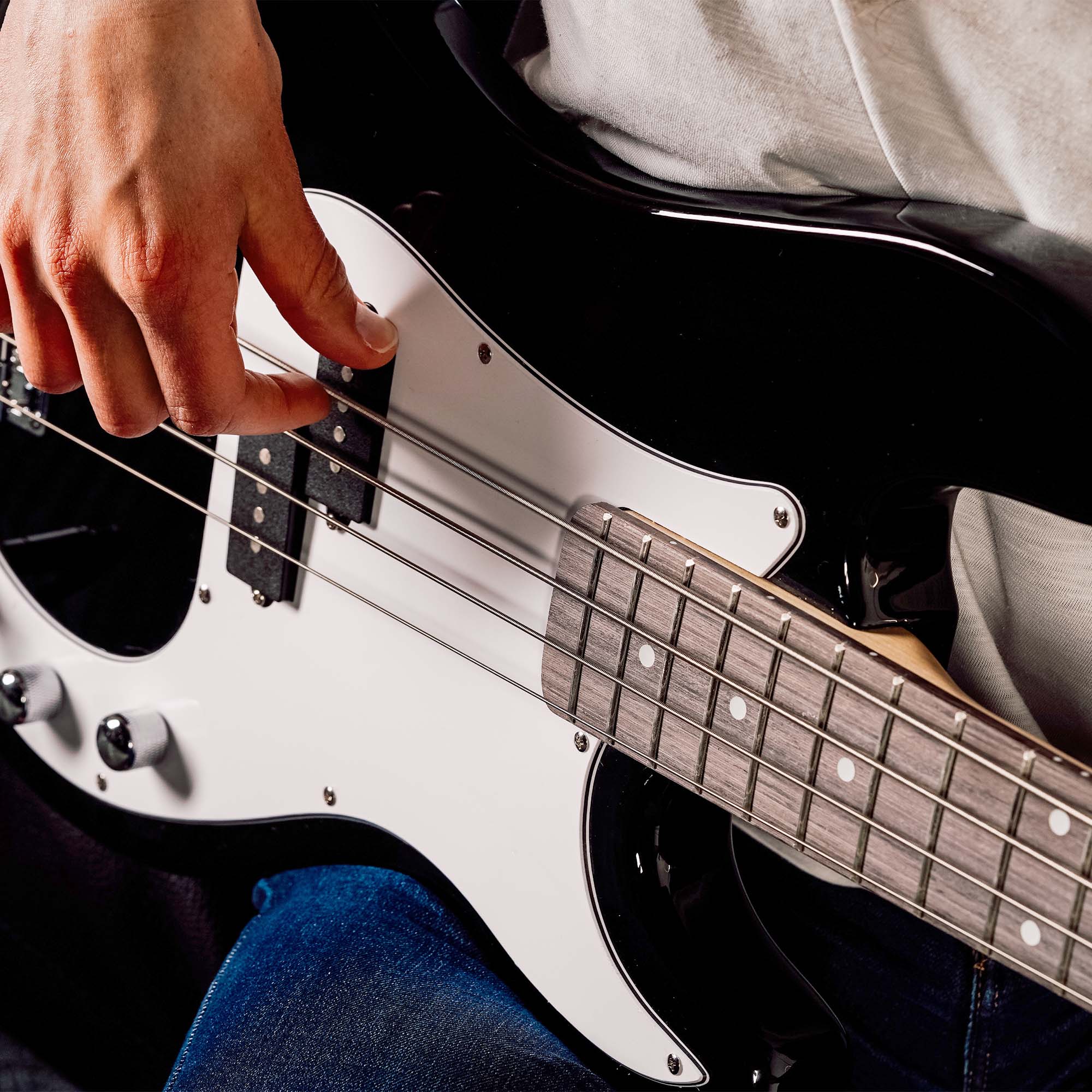 Hand plucking strings on a black electric bass guitar with light pickguard