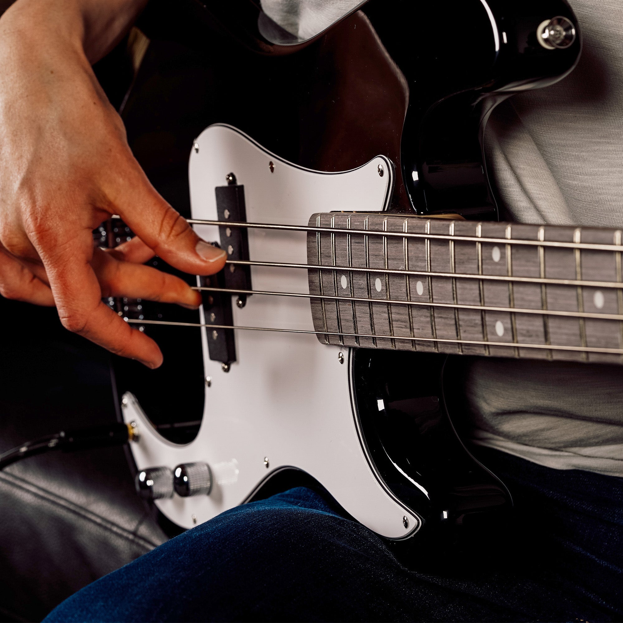 Hands fretting a black electric bass guitar with white pickguard