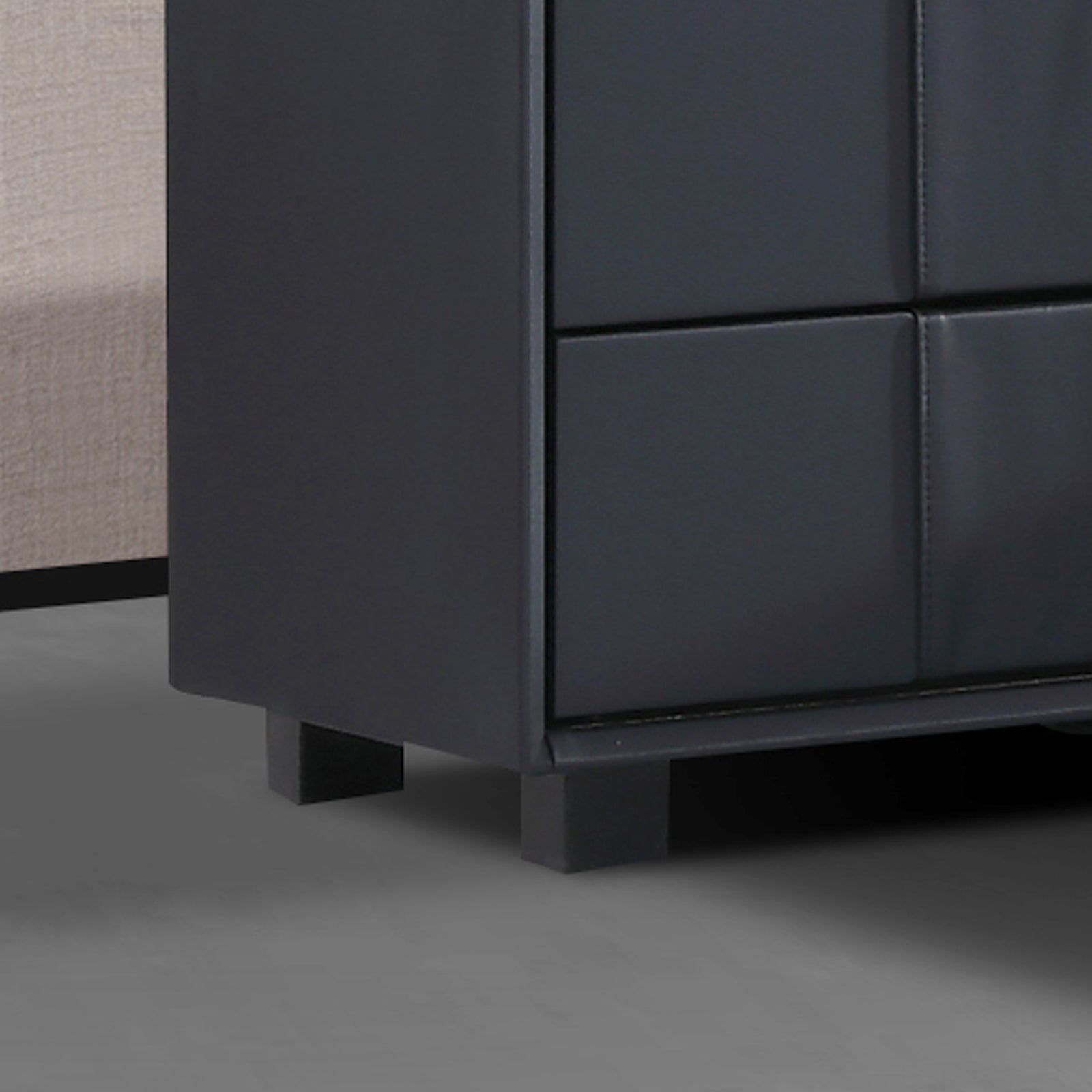 Dark upholstered bedside table corner with stitched drawer panels and block iron feet