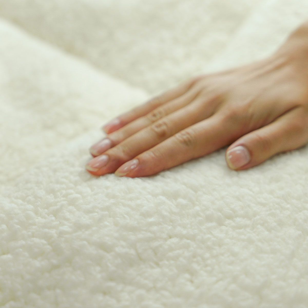 Cream sherpa mattress topper close-up with hand smoothing textured pile