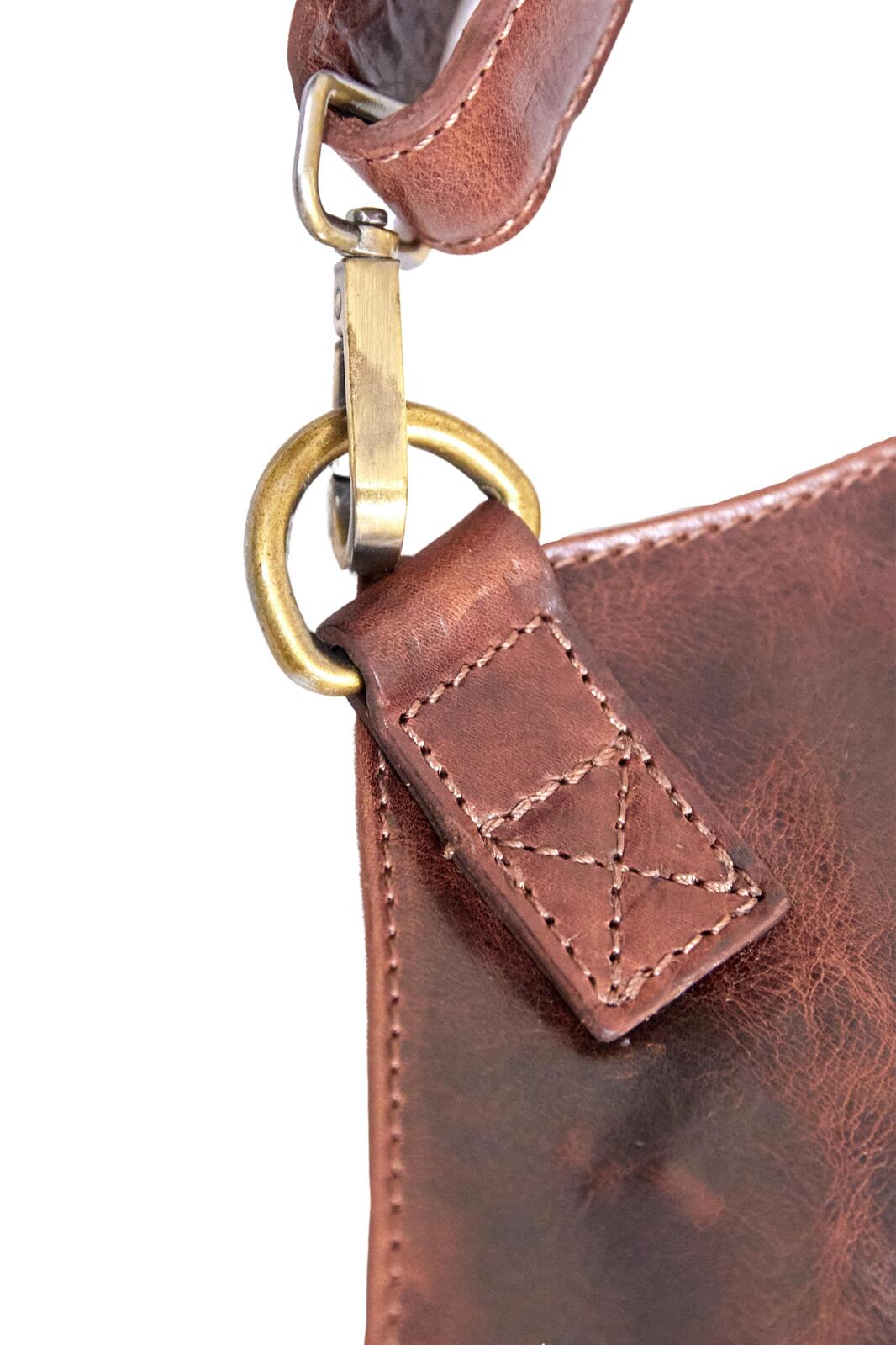 Close-up of metal snap and stitched leather cross-strap on a cognac apron