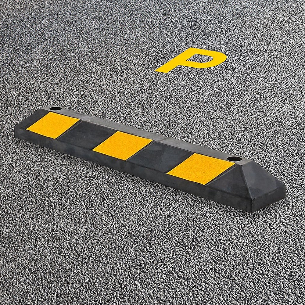 Black rubber wheel stop with yellow reflective pads on a textured surface