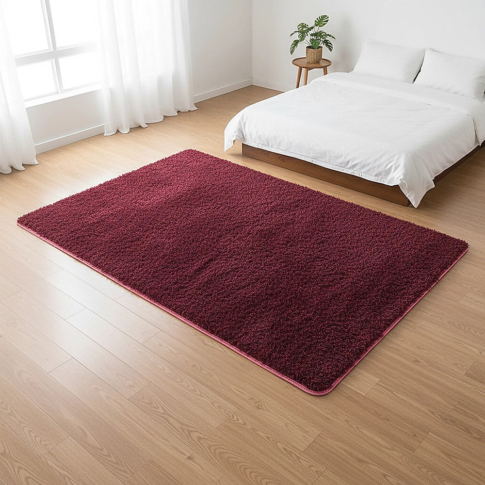 Burgundy shaggy rectangular area rug on wood floor, rounded corners visible