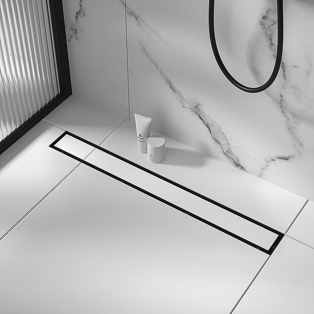 Black linear shower drain grate on tile floor, long channel with center outlet.
