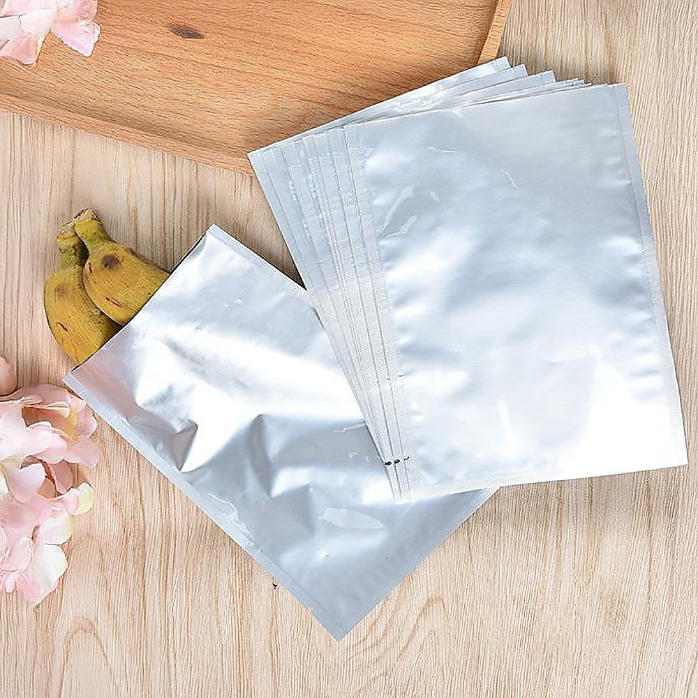 Set of silver Mylar vacuum storage pouches, multiple heat-seal bags laid on wood.